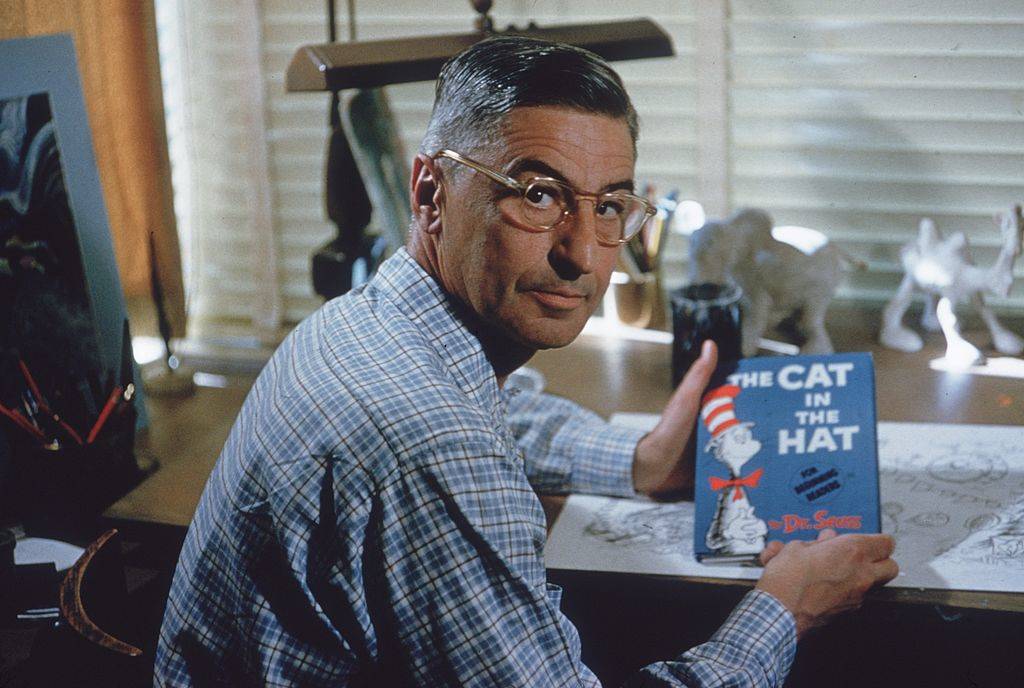 Dr. Seuss holding a copy of The Cat in the Hat at his drafting table