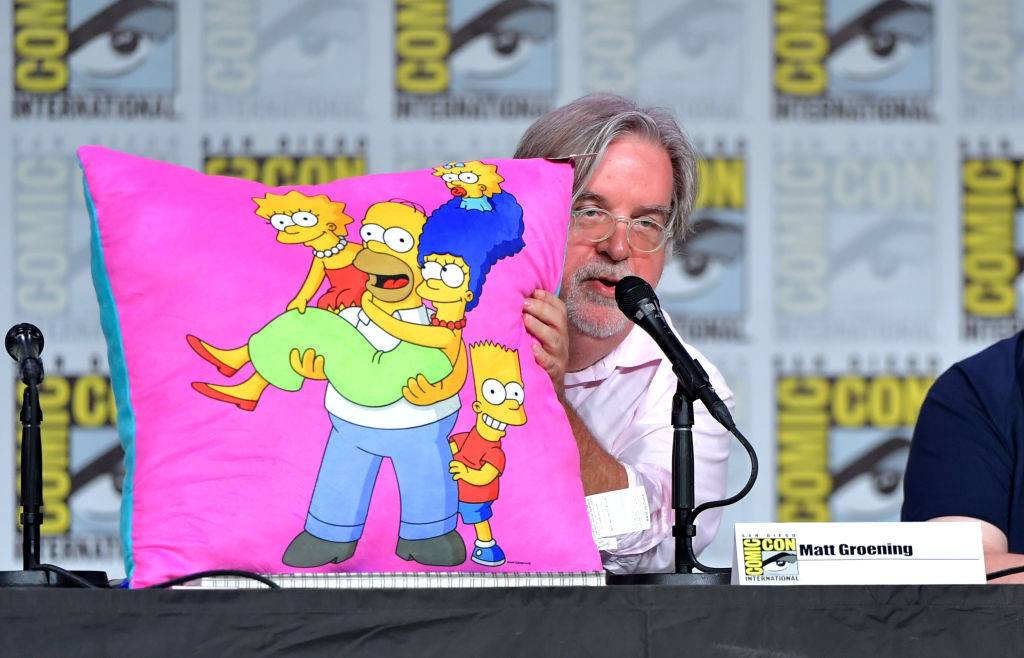 matt groening holding a pillow with The Simpsons characters on it during comic con