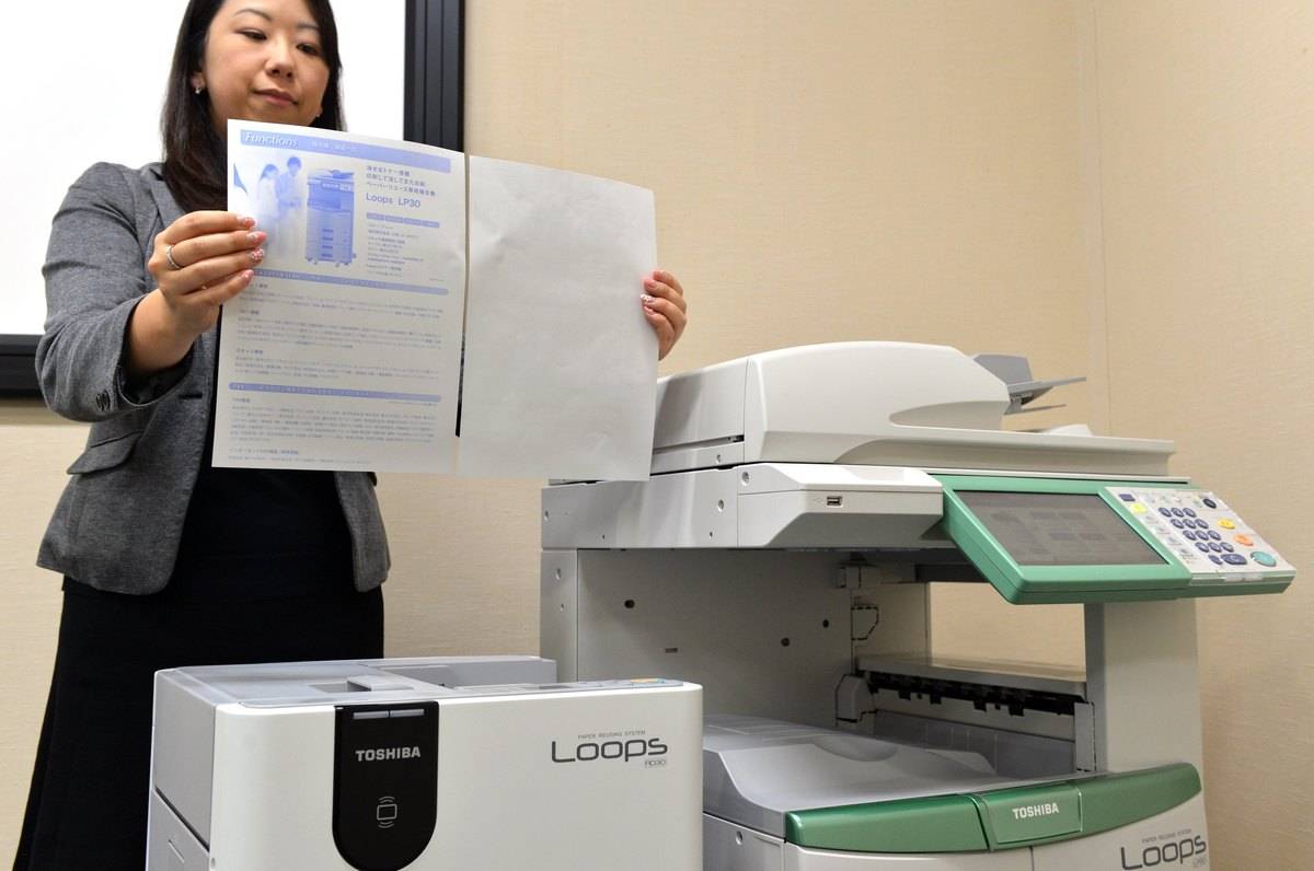 woman holding up two pieces of standard paper in front of printer
