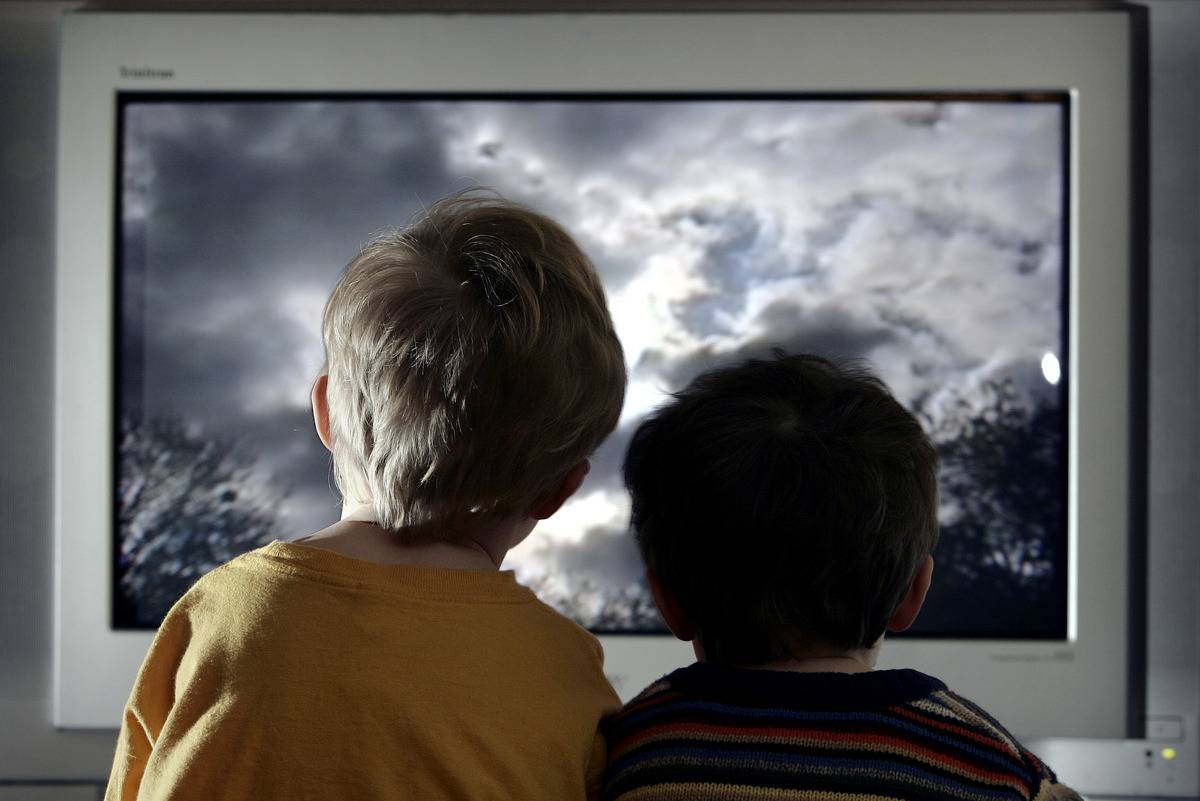 Two boys sit close to the TV.