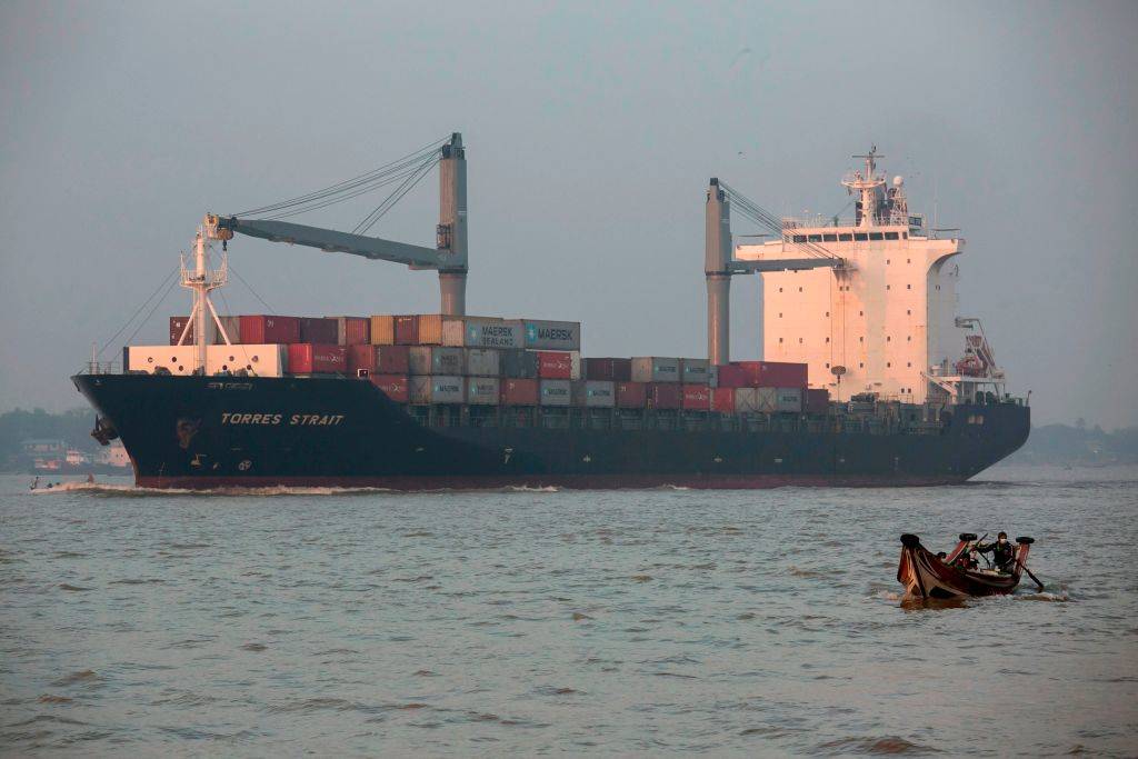 A man rides in a small boat past a container ship in the Yangon River