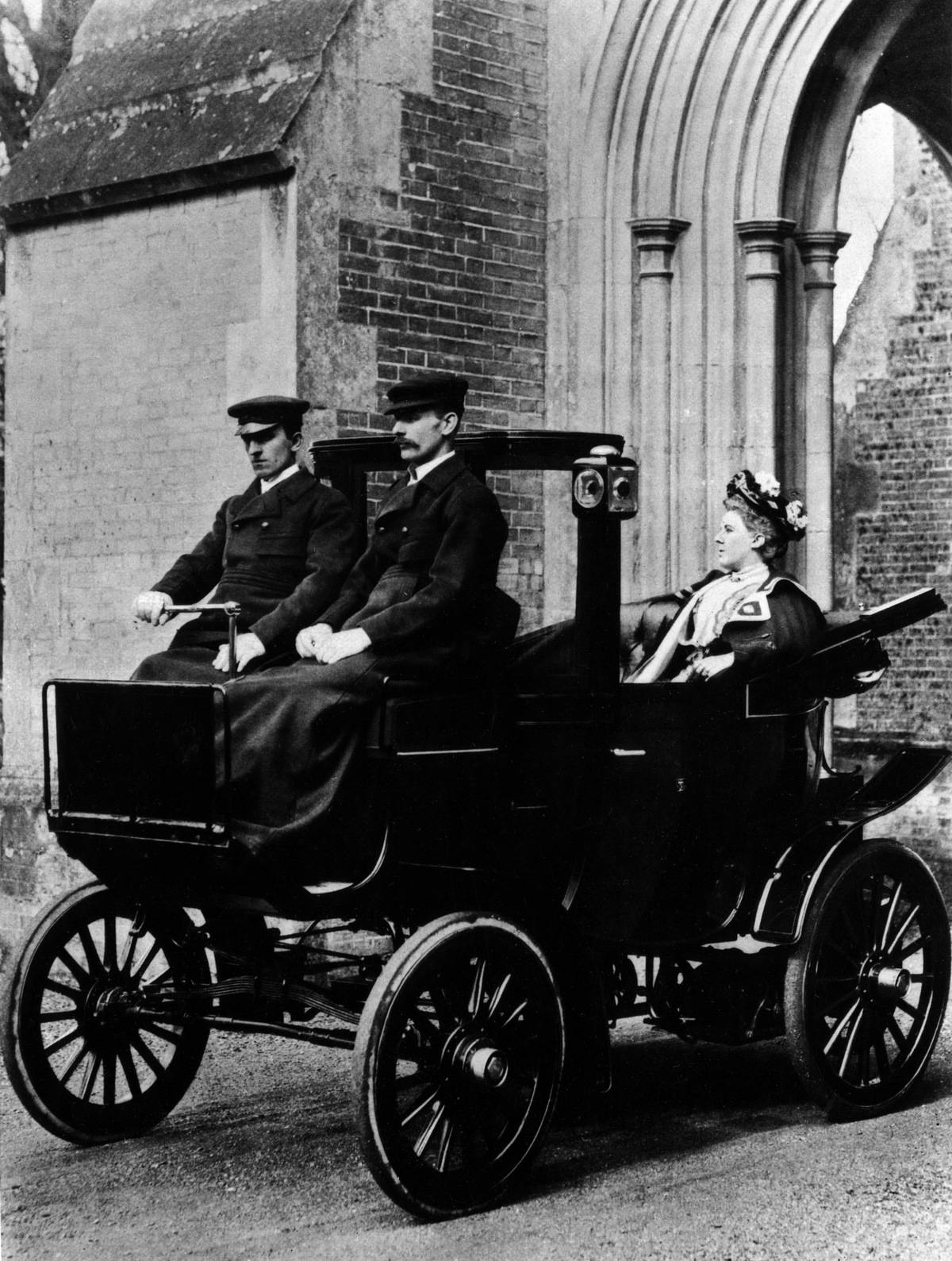 Two chauffeurs driving a convertible City and Suburban electric car.
