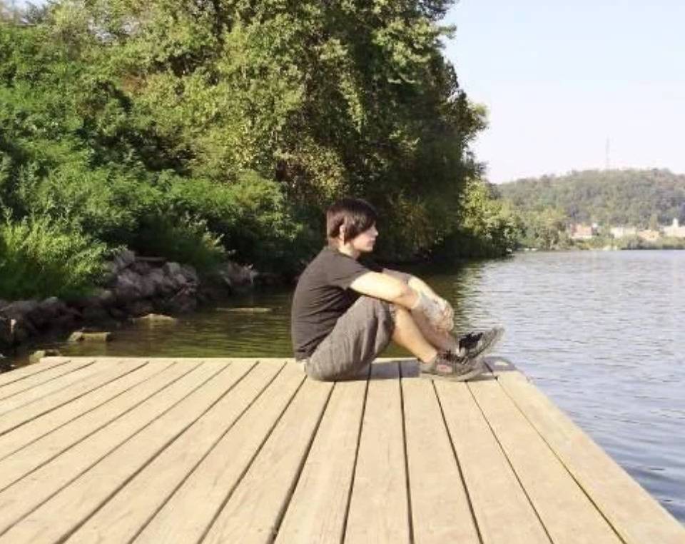guy with emo haircut sitting on dock dramatically looking over water