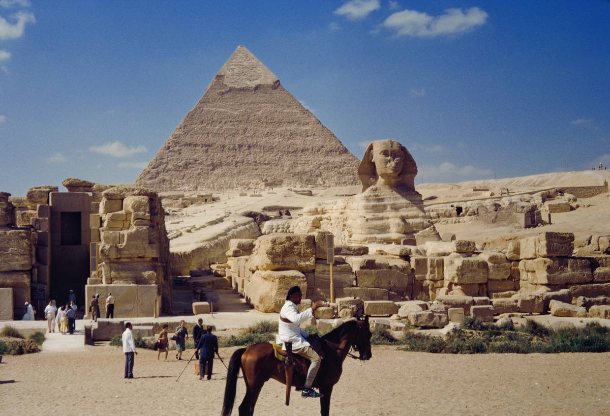 People on horseback are seen in front of a pyramid and the Sphinx.