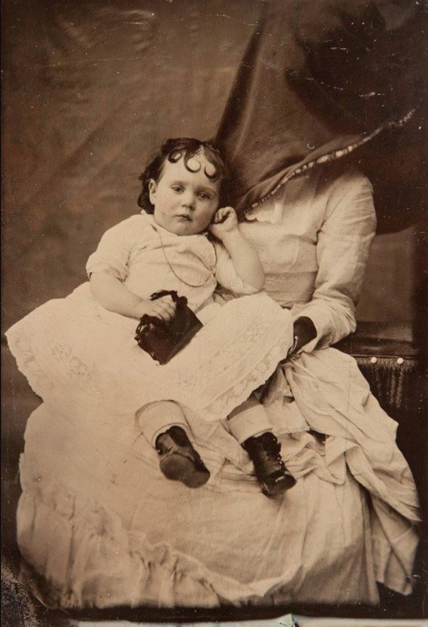 In this baby portrait, a mother's head is hidden behind a dark curtain.