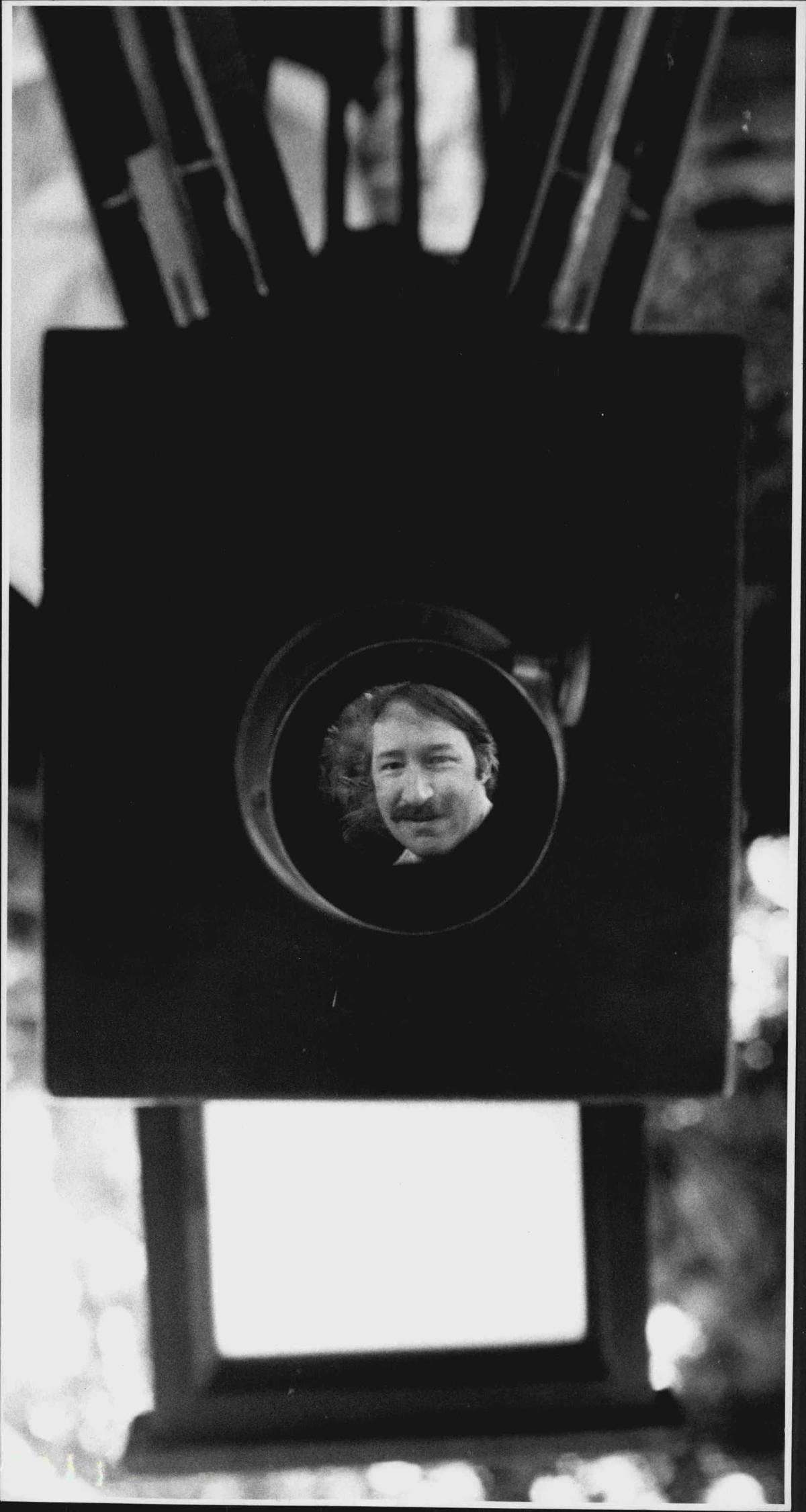 A man's reflection is in a daguerrotype camera.