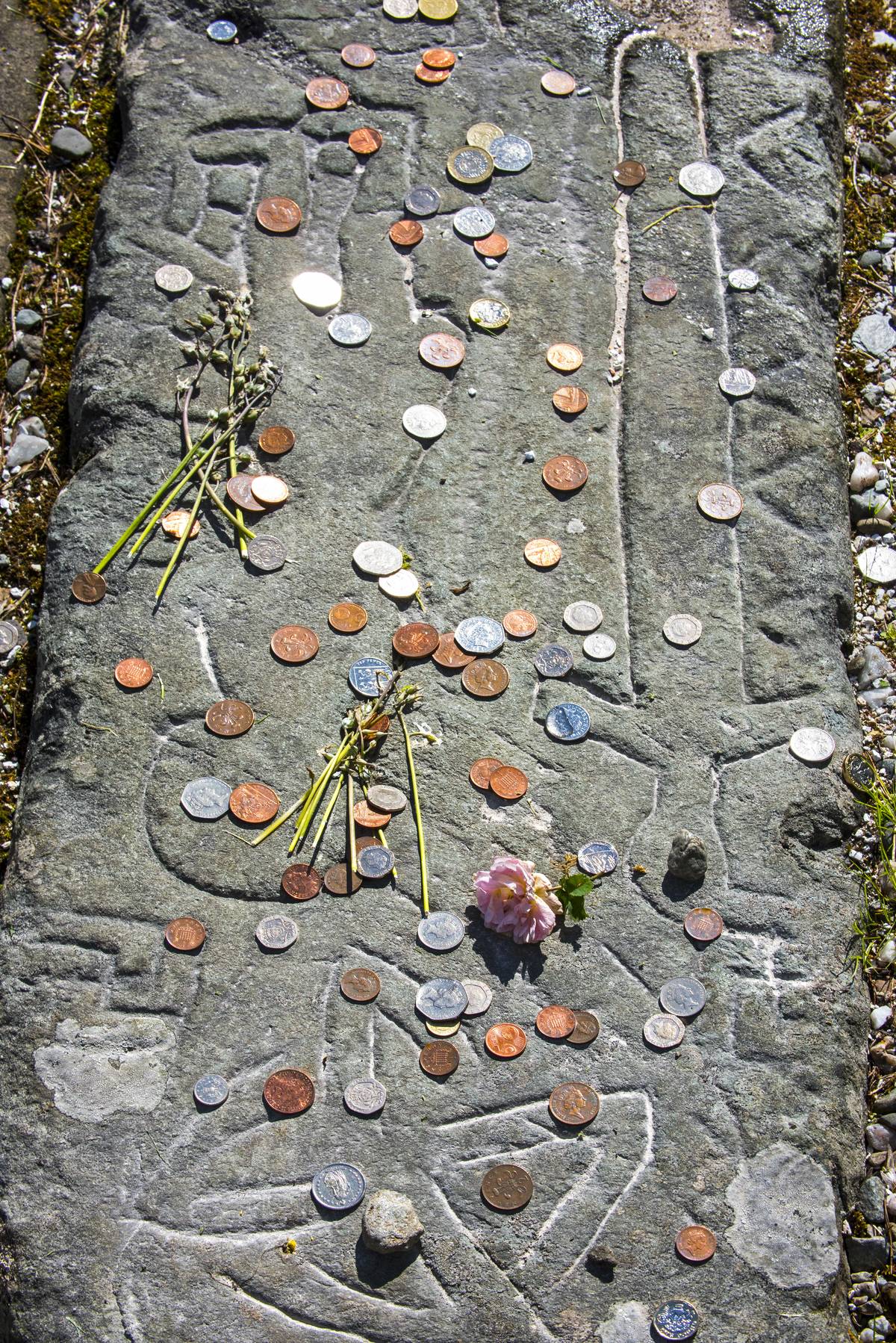 A variety of coins sit on a tombstone.