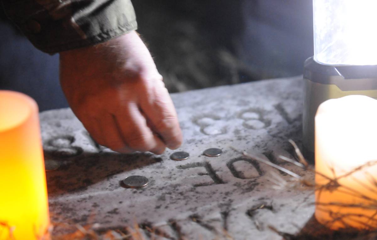 A visitor places coins on a grave marker.