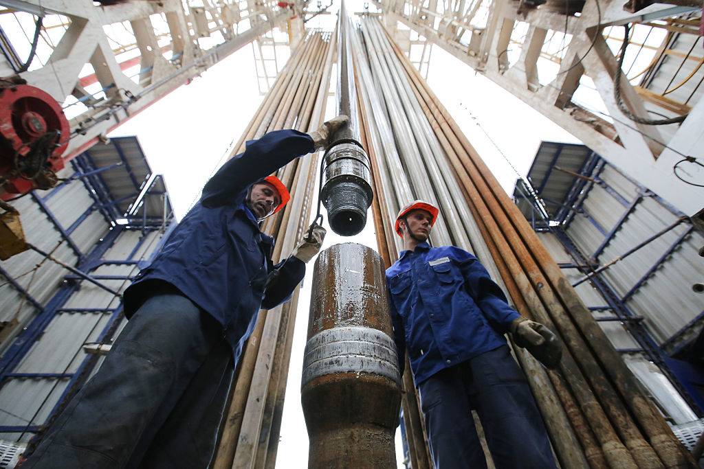 Workers secure drilling pipe sections on an oil drilling tower