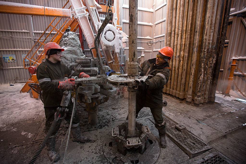 Workers use machinery to move drill sections on the drilling floor of the oil derrick