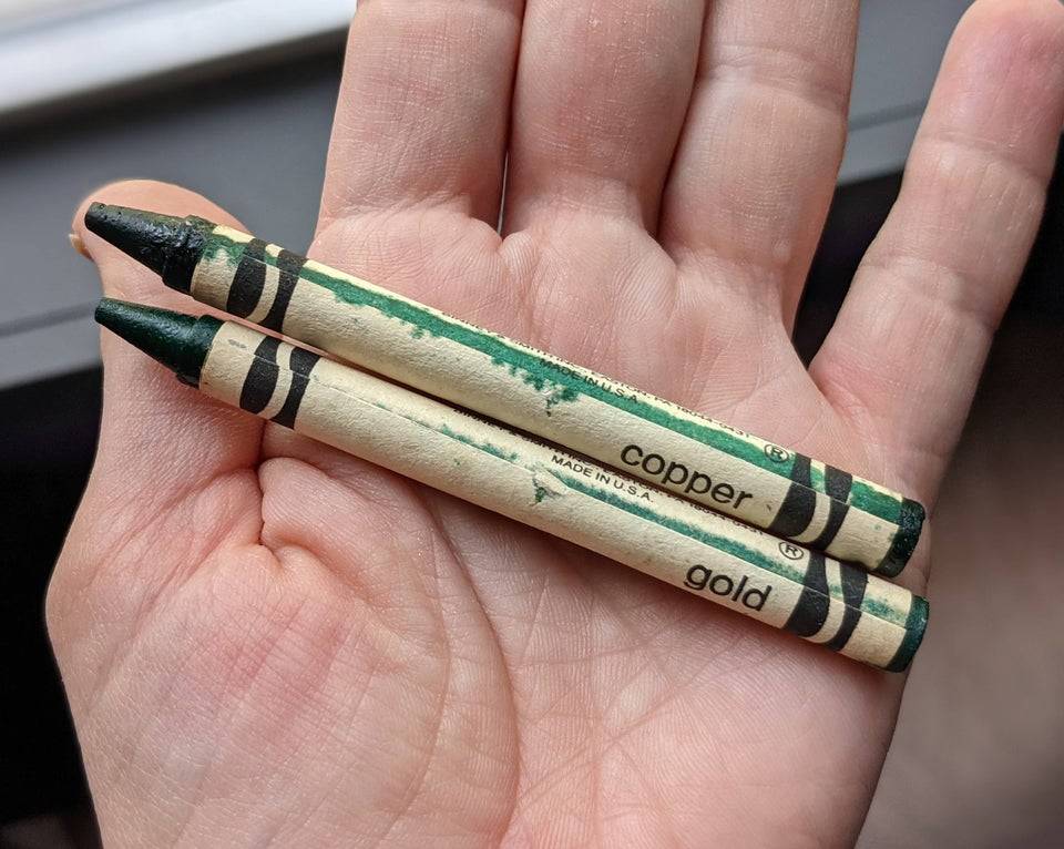 Outstretched hand holding gold and copper crayons that have oxidized over time and are now green