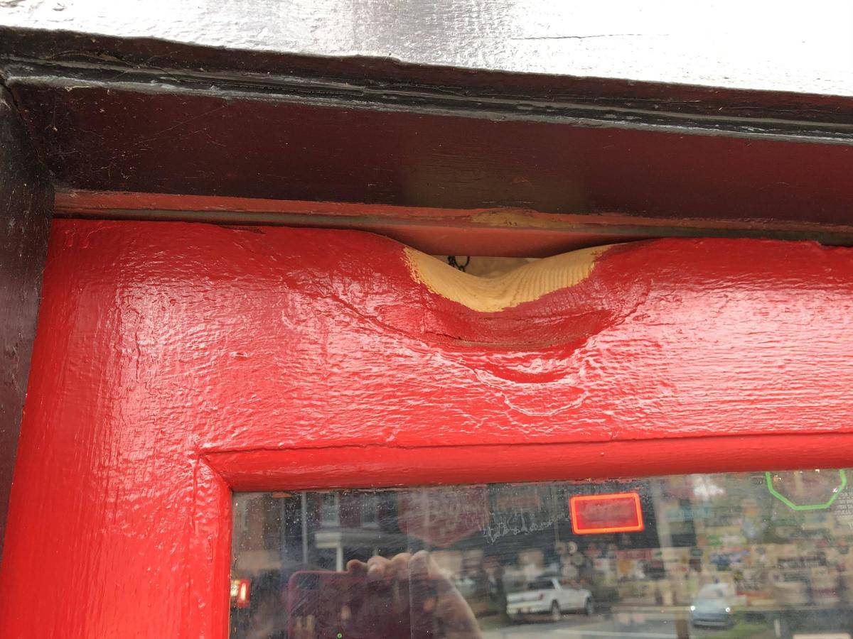 Wooden door painted red that is worn down at the top from 50 years of entry bell hitting it