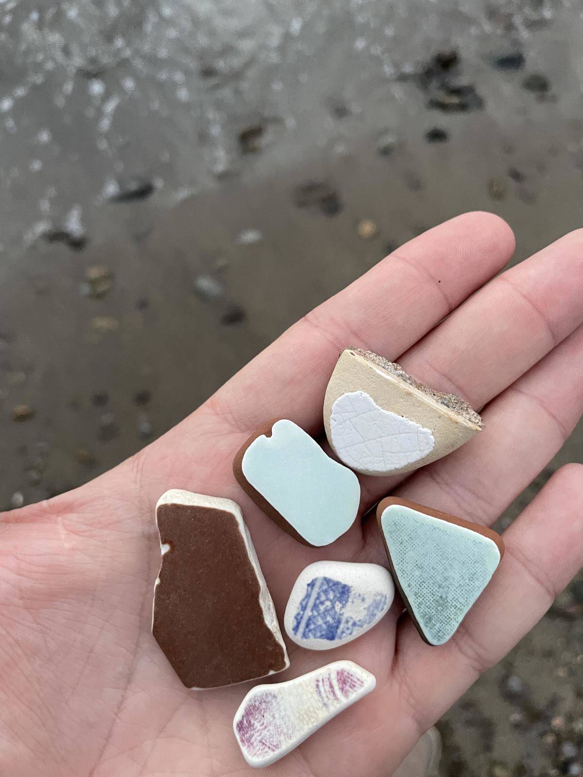 Outstretched hand holding sea glass and tiles worn down over time from ocean