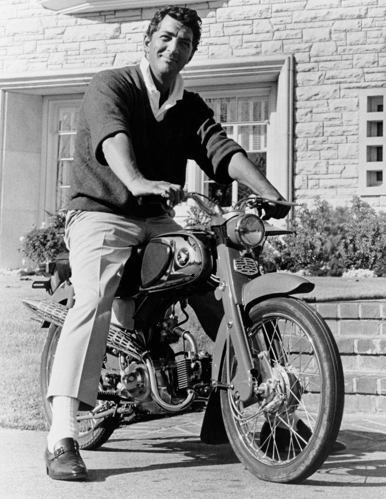 dean martin in front of his home on a motorcycle