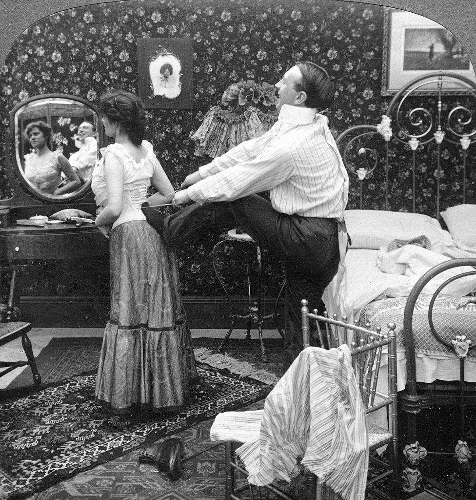 man tightening a woman's corset black and white photo