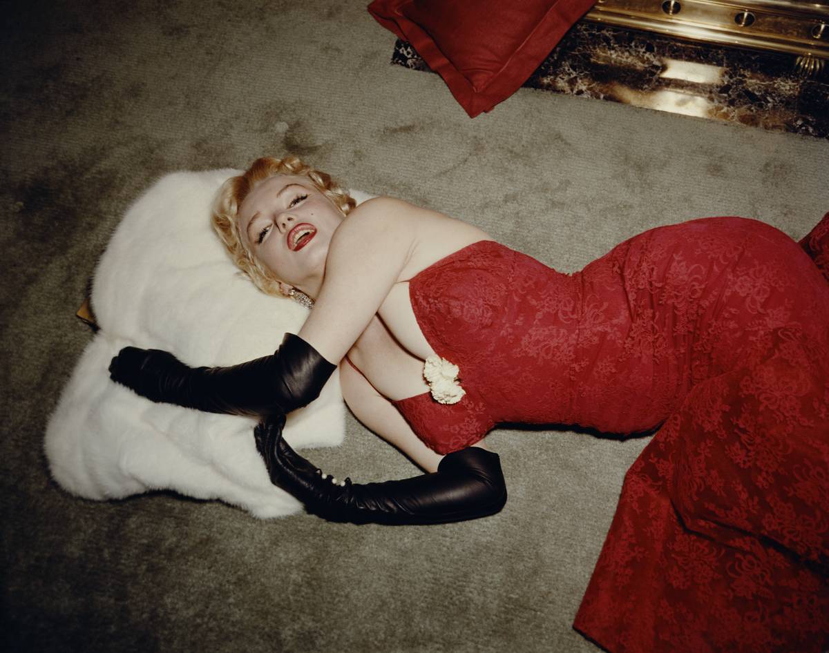 1955: EXCLUSIVE American actor Marilyn Monroe (1926 - 1962), wearing a red brocade evening gown and long black gloves, lying on a carpet and
using a white fur stole as a pillow.