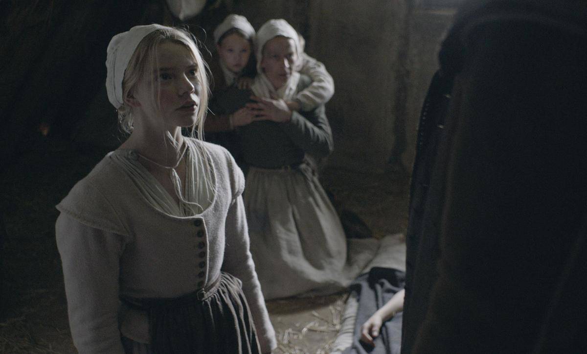 Anya Taylor Joy standing in front of huddled women in The Witch