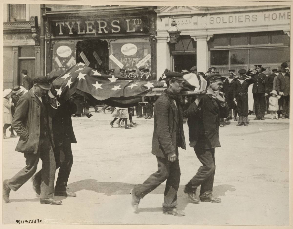 Four men carry the American flag-covered cover the body of victim  recovered from the RMS Lusitania as it is carried past saluting military
 and members of the public on the way to a temporary morgue, Queenstown 
(later known as Cobh), Ireland, May 1915.