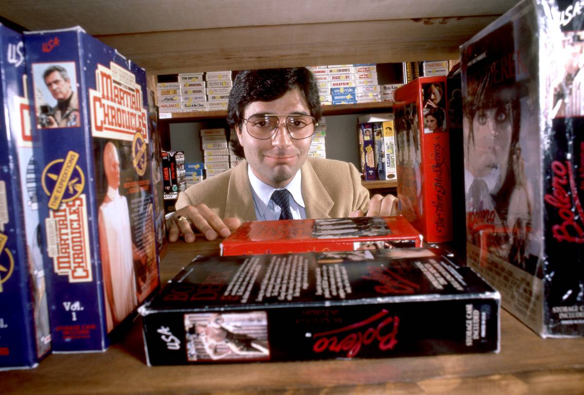 Video store owner Jimmy Russo poses for a portrait behind a bookshelf with VHS tapes circa September, 1985 in Los Angeles, California.