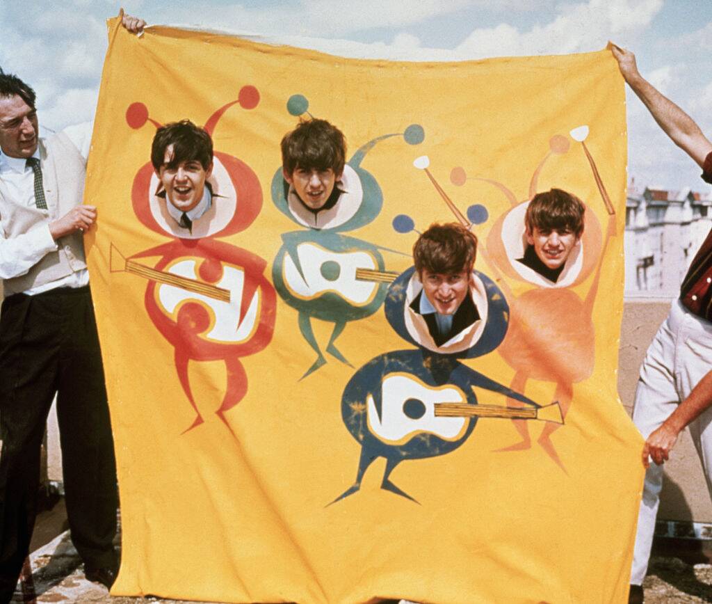 The Beatles poke smiling faces out of a banner drawn with beatle bodies holding guitars in the early part of their band's career