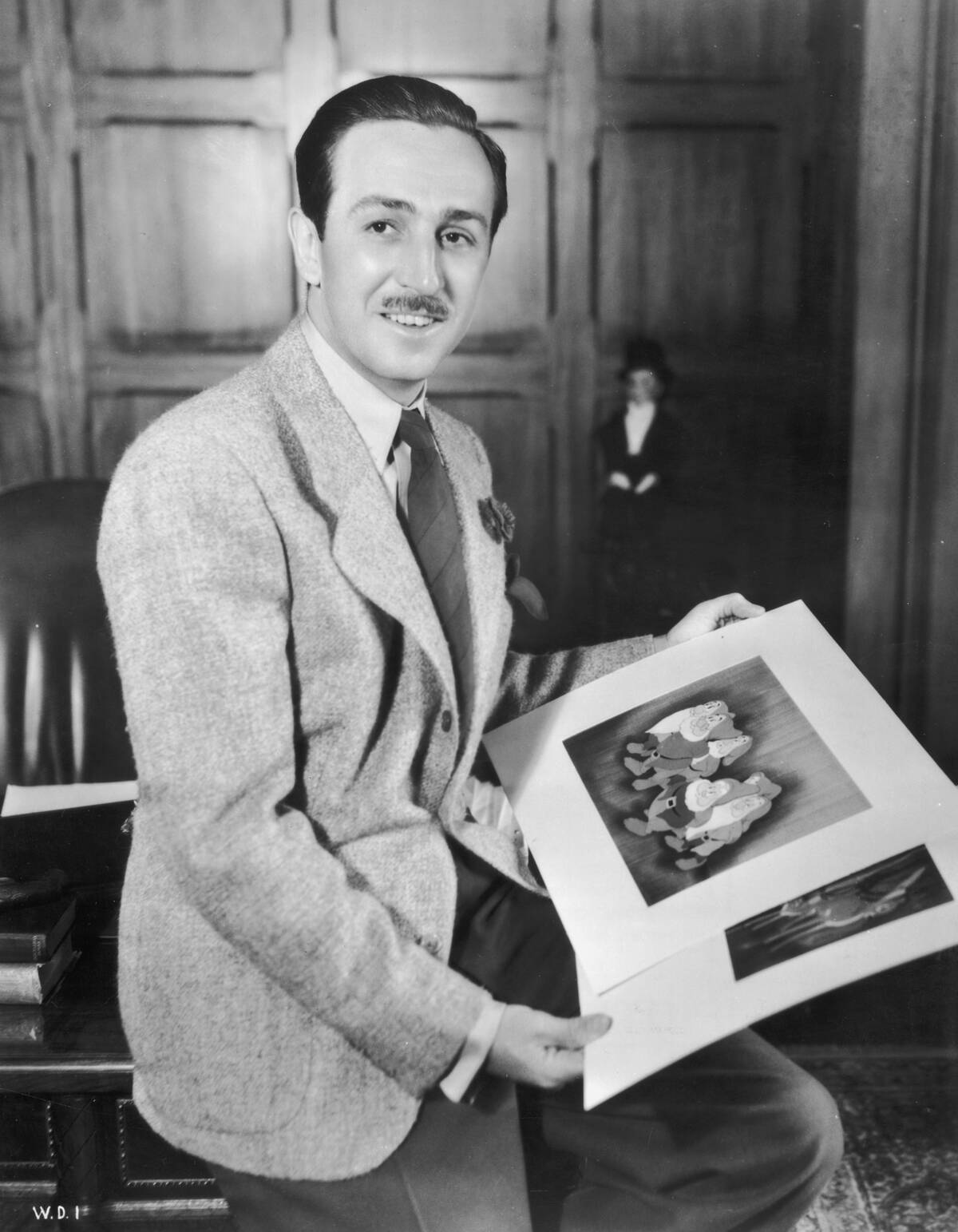 A portrait of American cartoonist and producer Walt Disney (1901 - 1966) seated on the edge of a desk in an office holding illustrations from
his animated films 'Snow White and the Seven Dwarfs' and 'Bambi.'
Animator David Hand directed both films.