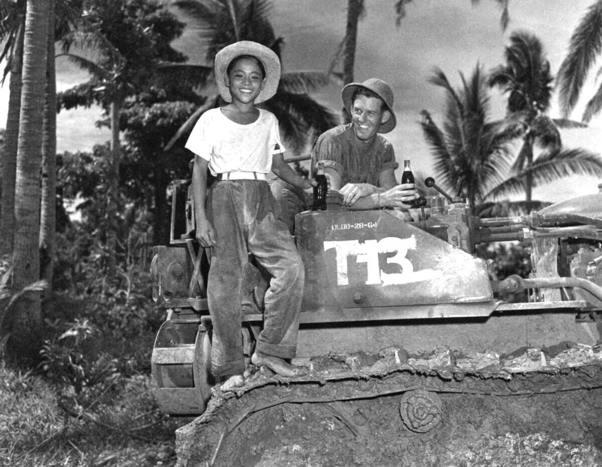 Philippines/USA: A young Filipino boy and an American bulldozer operator of the 64th Seabees (United States Naval Construction Forces, or NCF) enjoy a cold drink following the Battle of Samar, Leyte Gulf Campaign, October 1944.