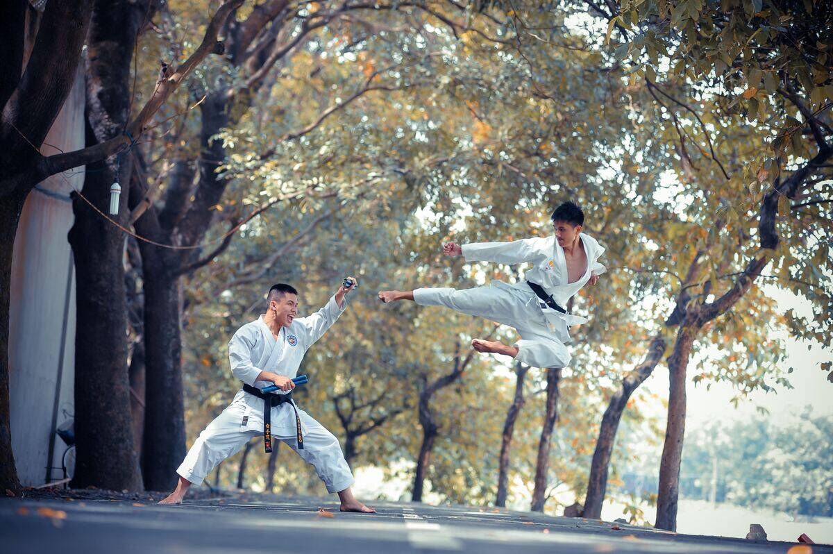 Man in gi holding nunchaku while screaming as another man in a gi performs a flying kick