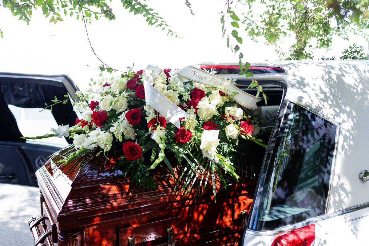 casket adorned with flowers being loaded into hearse