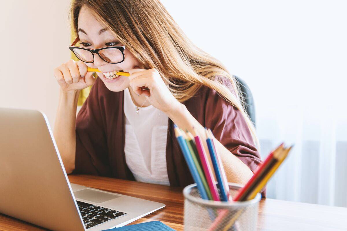 woman in glasses biting down on pencil in front of laptop