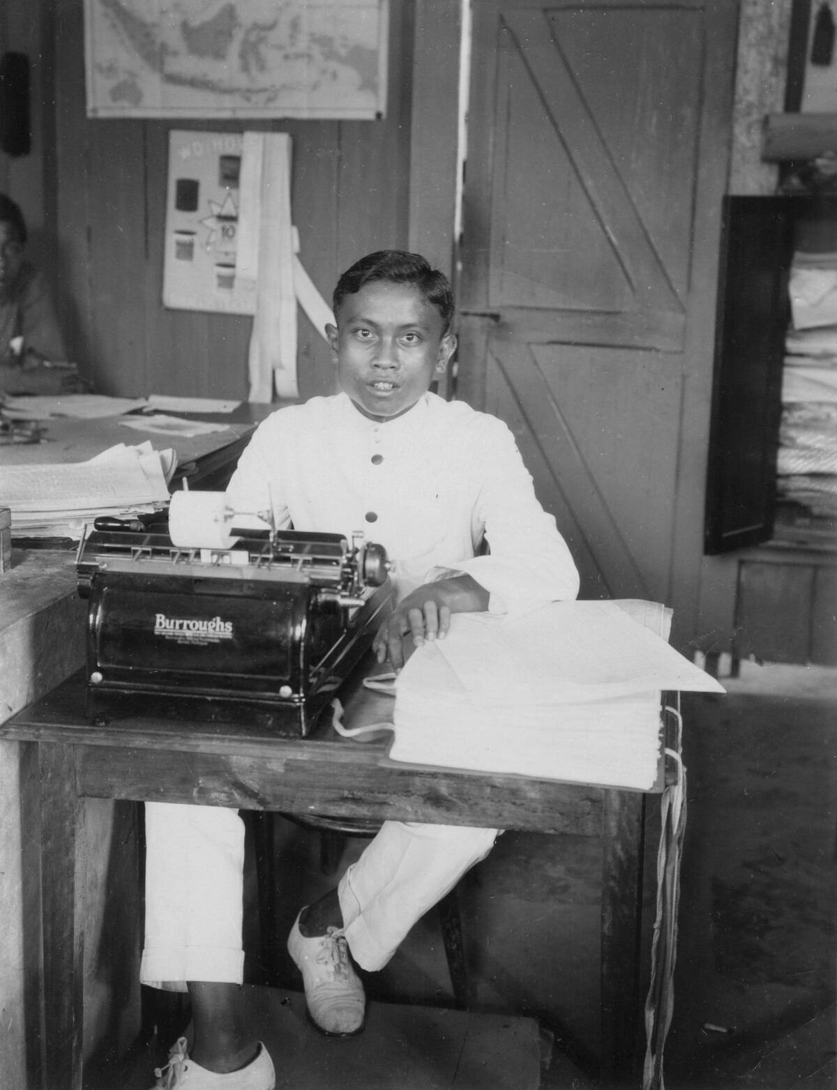 A young man sitting at a typewriter, Indonesia, 20th century.