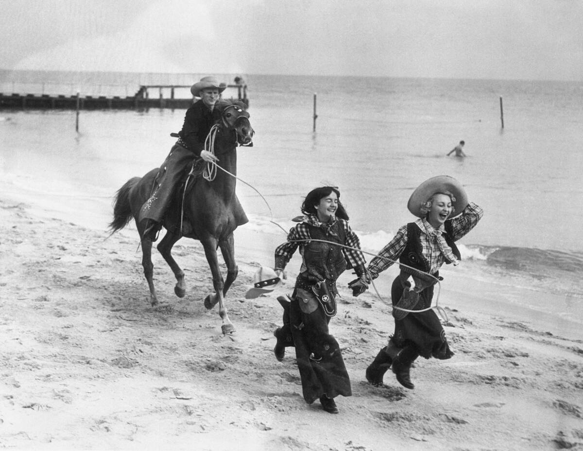 Cowboy on horse catching laughing women on beach