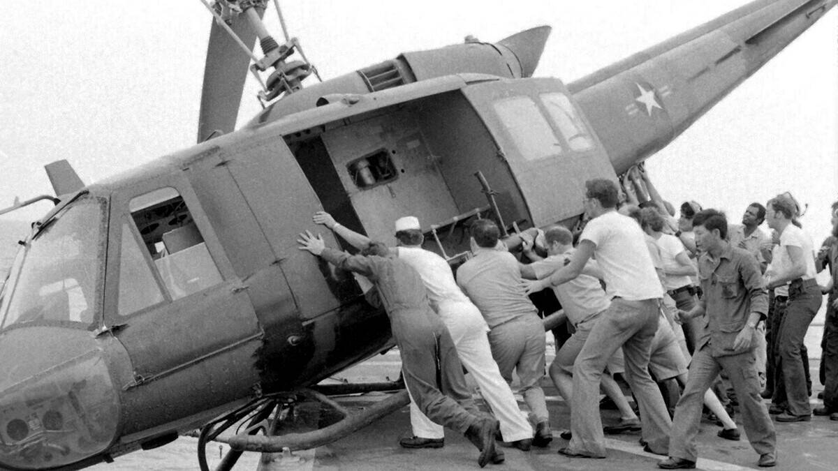 Vietnam: US Navy personnel struggle to push an army Huey helicopter off the deck of a US Navy carrier to make room for more refugee flights. Fall of Saigon, 29 April 1975