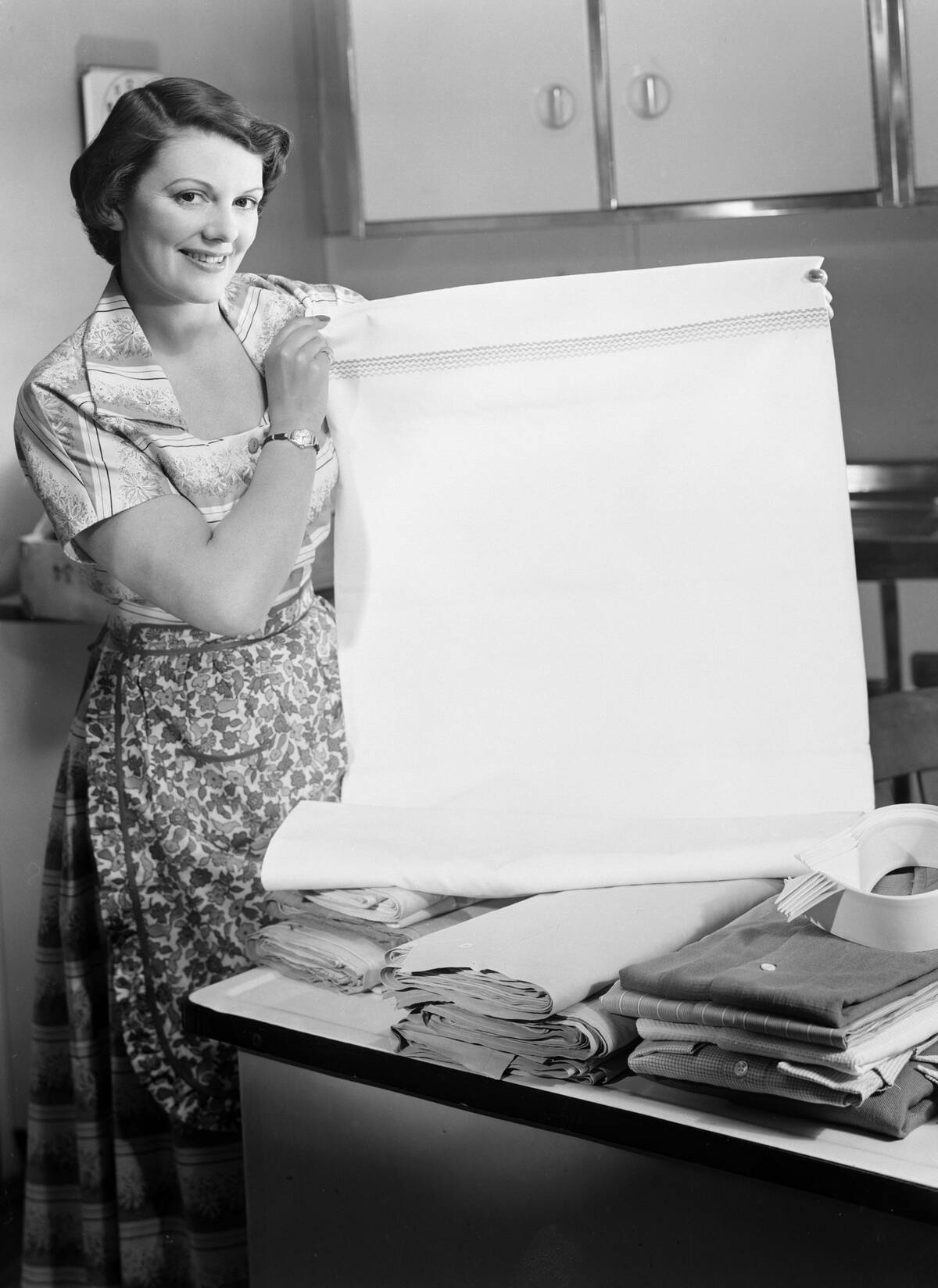 Woman holding a freshly laundered sheet, 1950.