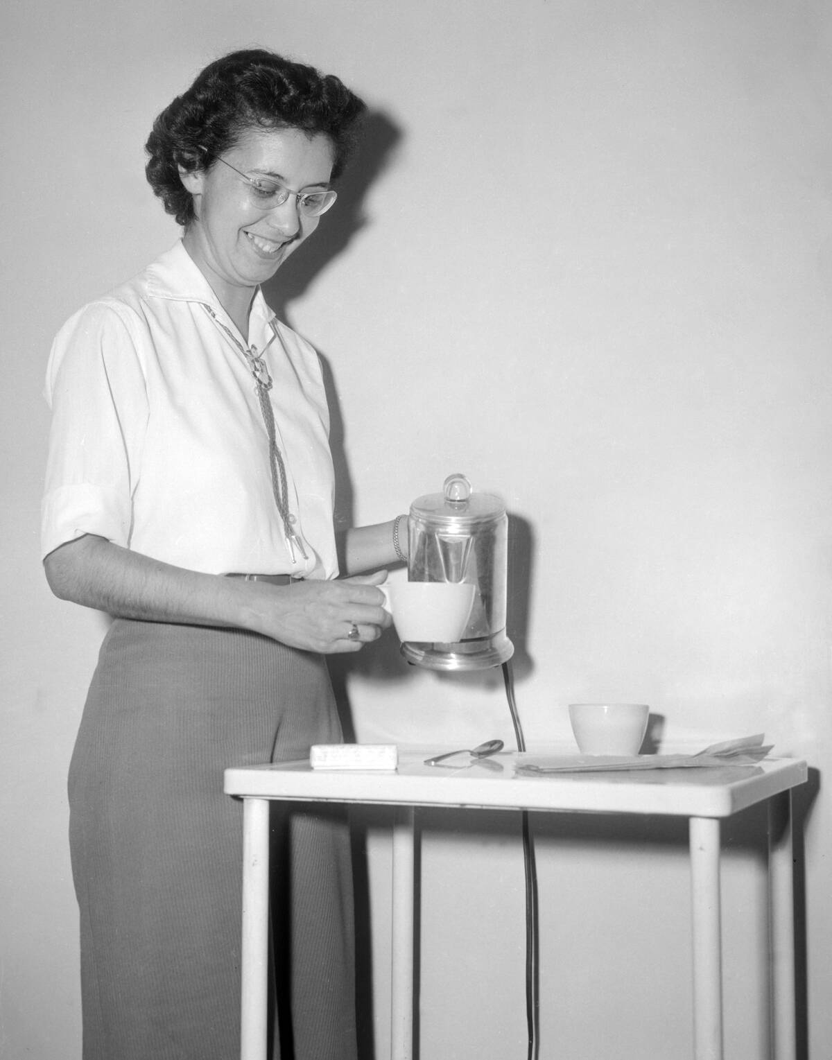 A woman pours a cup of coffee from a percolator, ca. 1960.