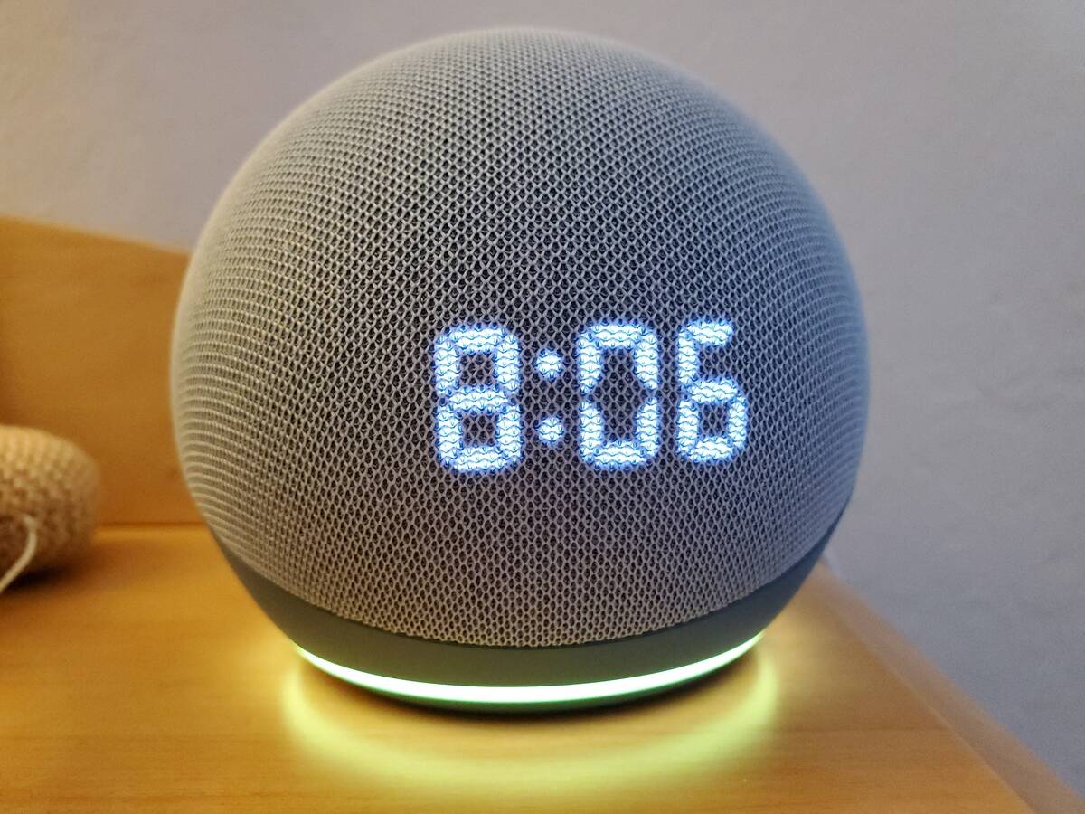 Amazon Echo Dot displaying 8:06 as the time. It's lit at the bottom, with the light bouncing off the wooden table it's atop