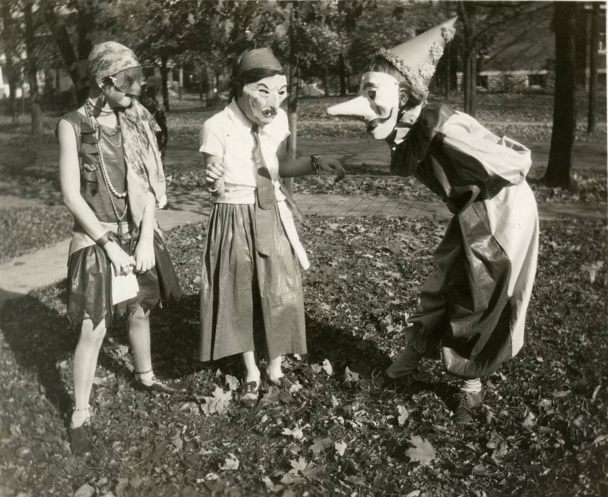Three girls wearing masks and in costume stand outside and converse with each other