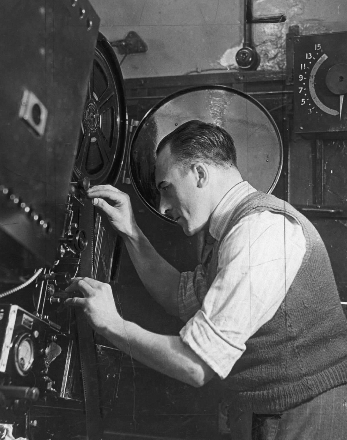 A projectionist threads a roll of film onto the projector, March 1938