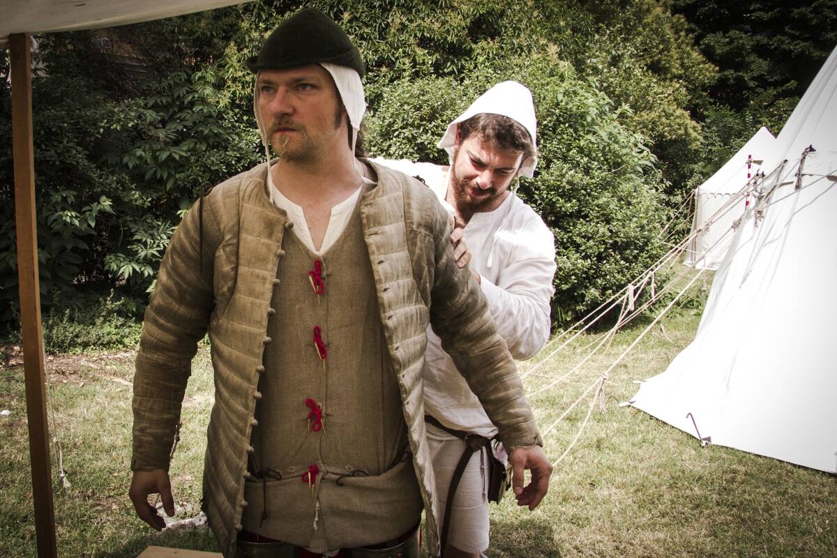 A squire helping a knight to put on his gambeson...