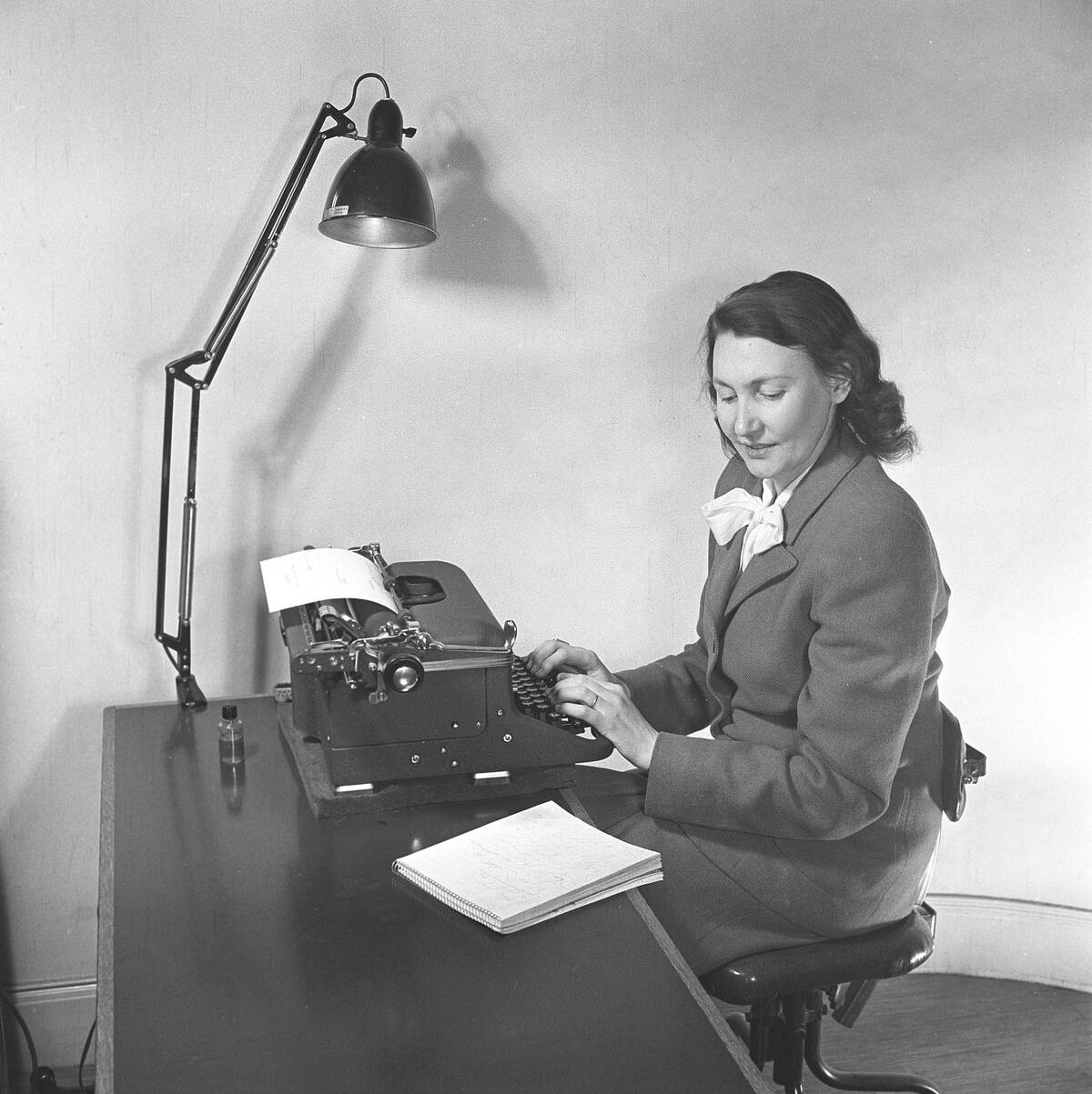 Office girl in the 1940s. A woman is sitting at a office desk typing on her typewriter a text from ano...
