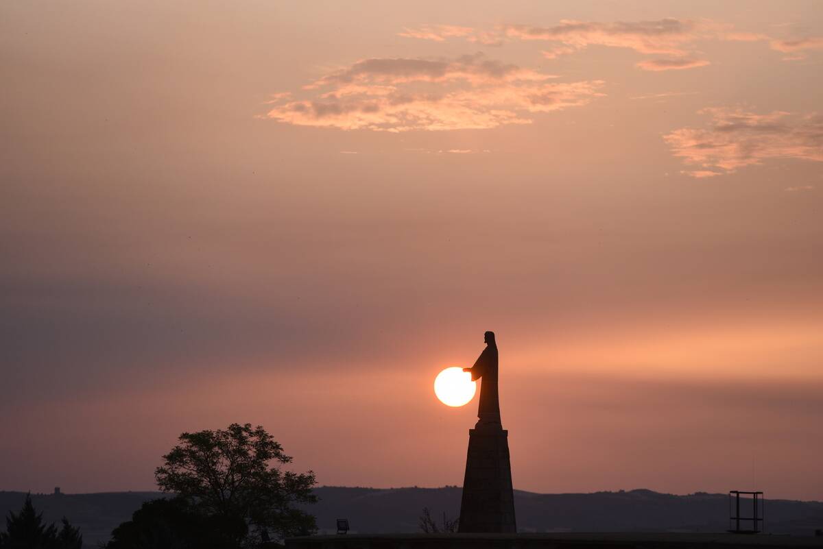 The sun rises behind a statue of Jesus Christ in Almazán in...