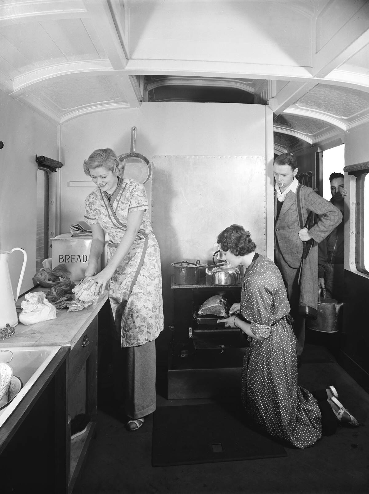 Holidaymakers preparing food inside a camping coach, 1936.