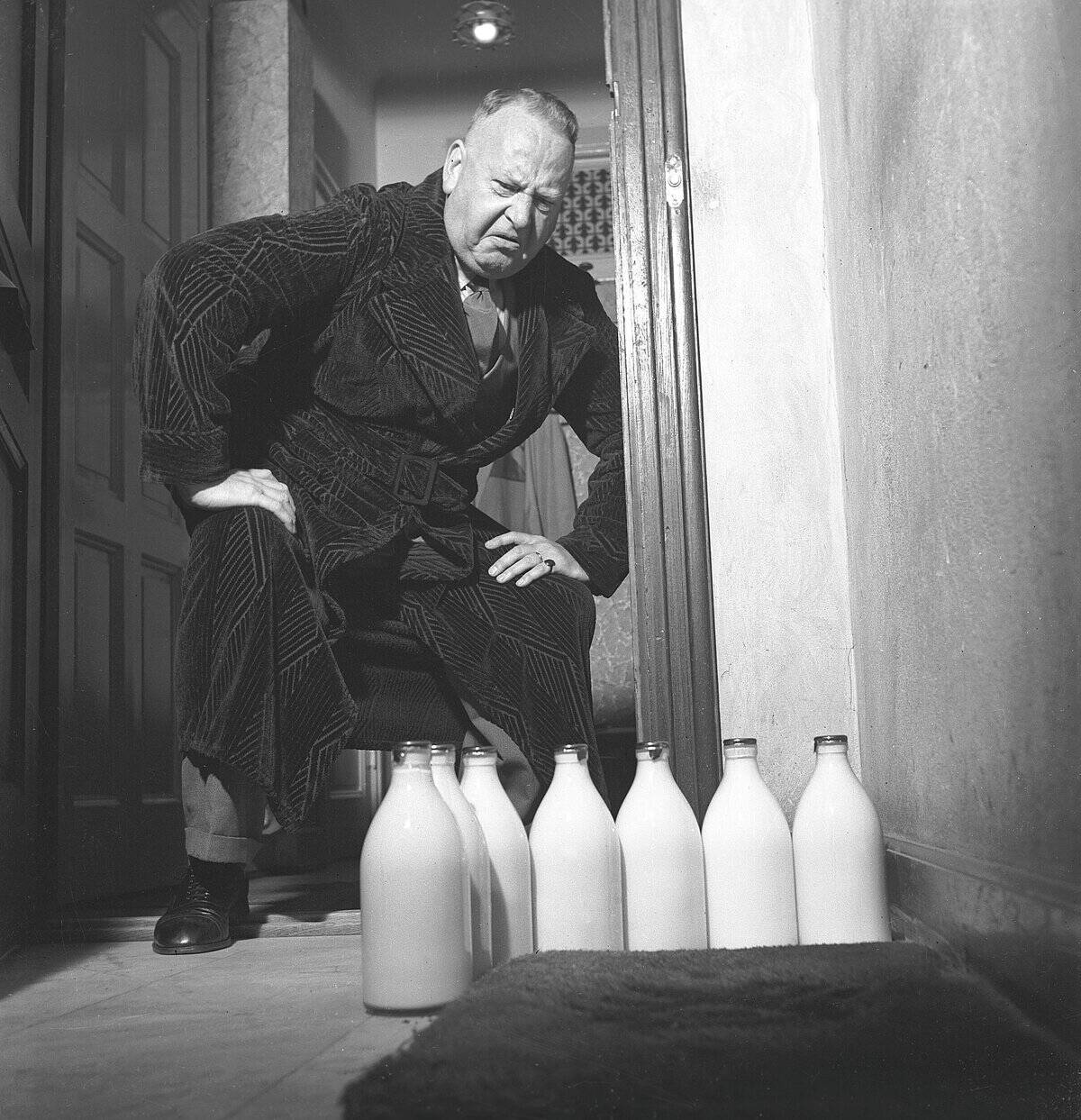 Man of the 1940s. A man visibly disapointed over the several milk bottles standing on his doorstep. He...