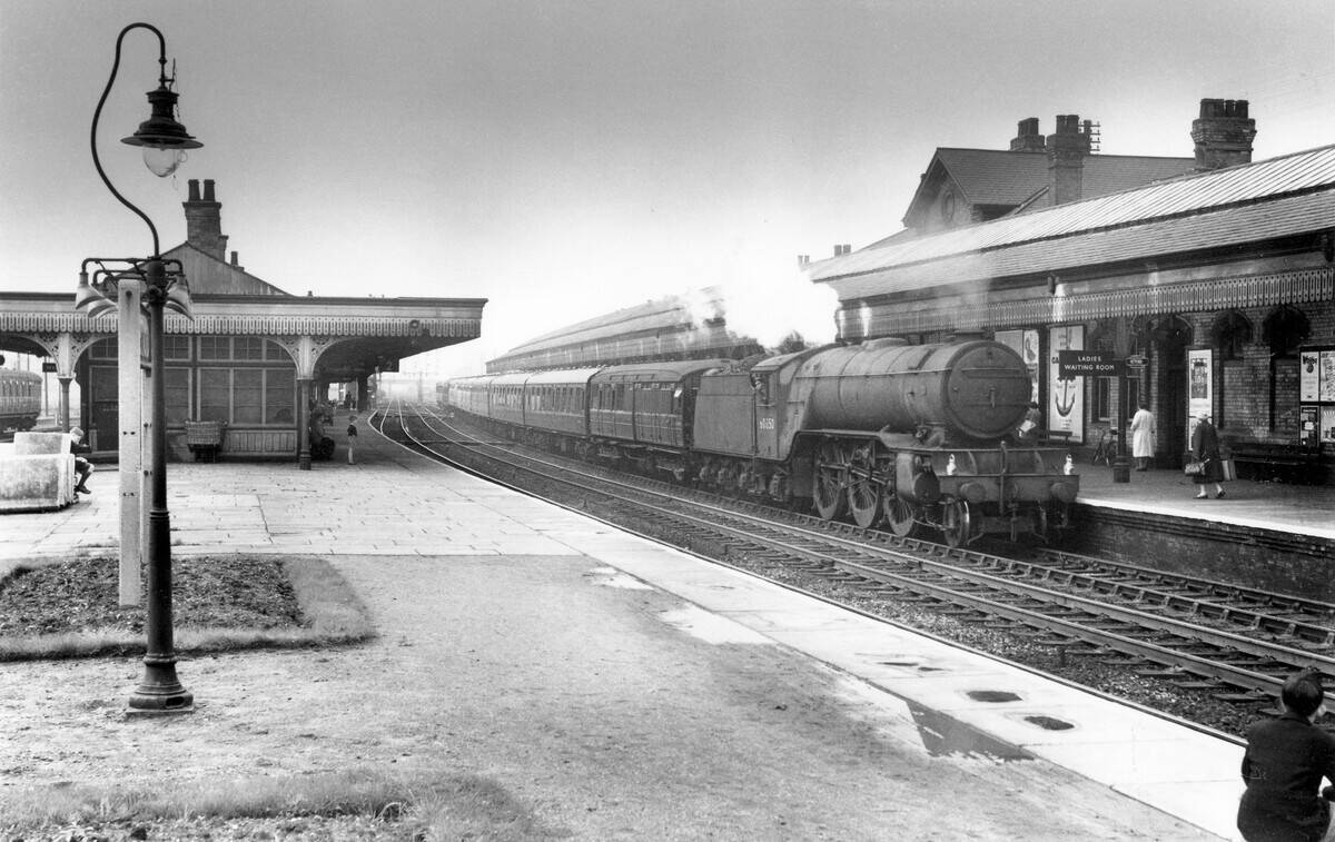 The low canopy building of Retford station on the East Coast Main Line is host to Gresley V2 Class 2-6-2 No.60850 intently being watched by three boys. C1960.