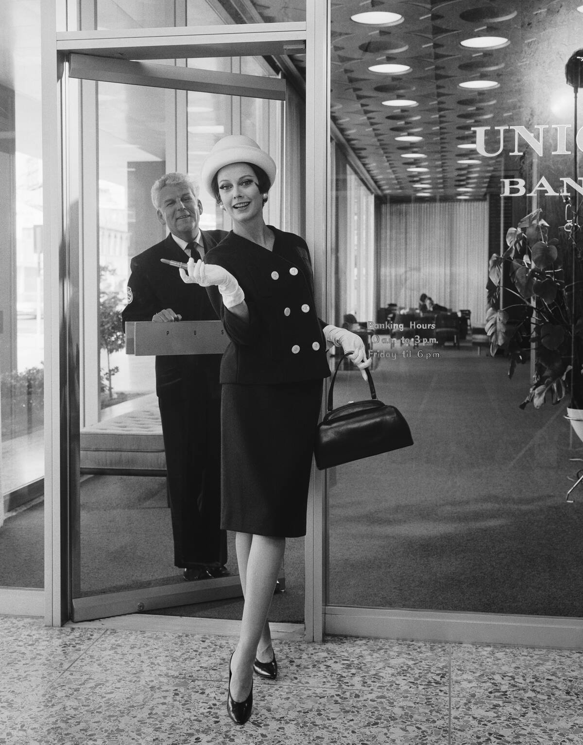Woman standing in front of bank door, man in background