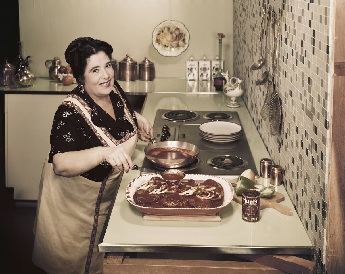Mature woman pouring tomato paste on meat, smiling, portrait