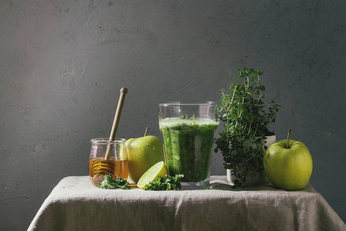 Green spinach kale apple honey smoothie in glass on linen table cloth with ingredients above. Healthy organic eating.