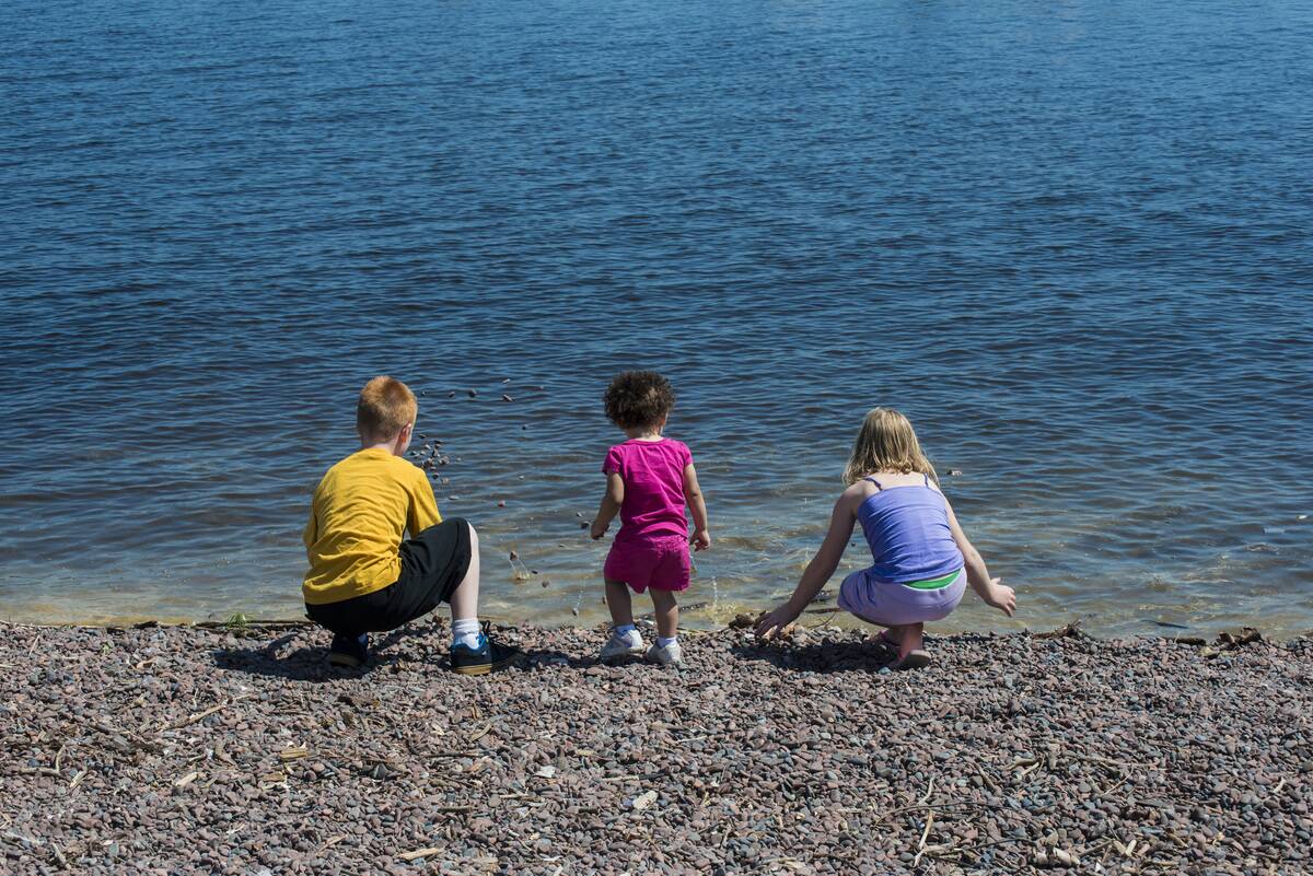 Three siblings, one of them bi-racial having fun skimming rocks into the lake on vacation
