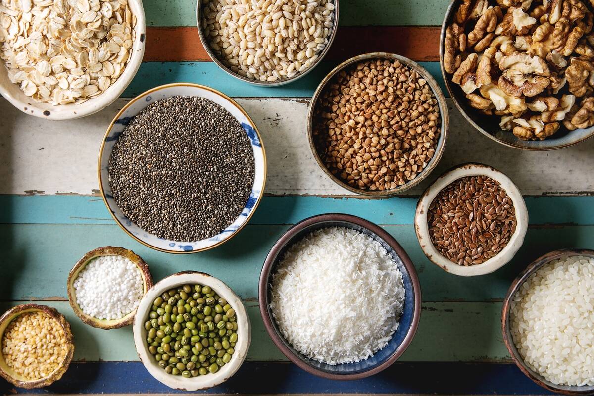 Variety of raw uncooked grains superfood cereal chia seeds. sesame. mung bean. walnuts. tapioca. wheat. buckwheat. oatmeal. coconut. rice in ceramic bowls. Wooden plank background. Flat lay