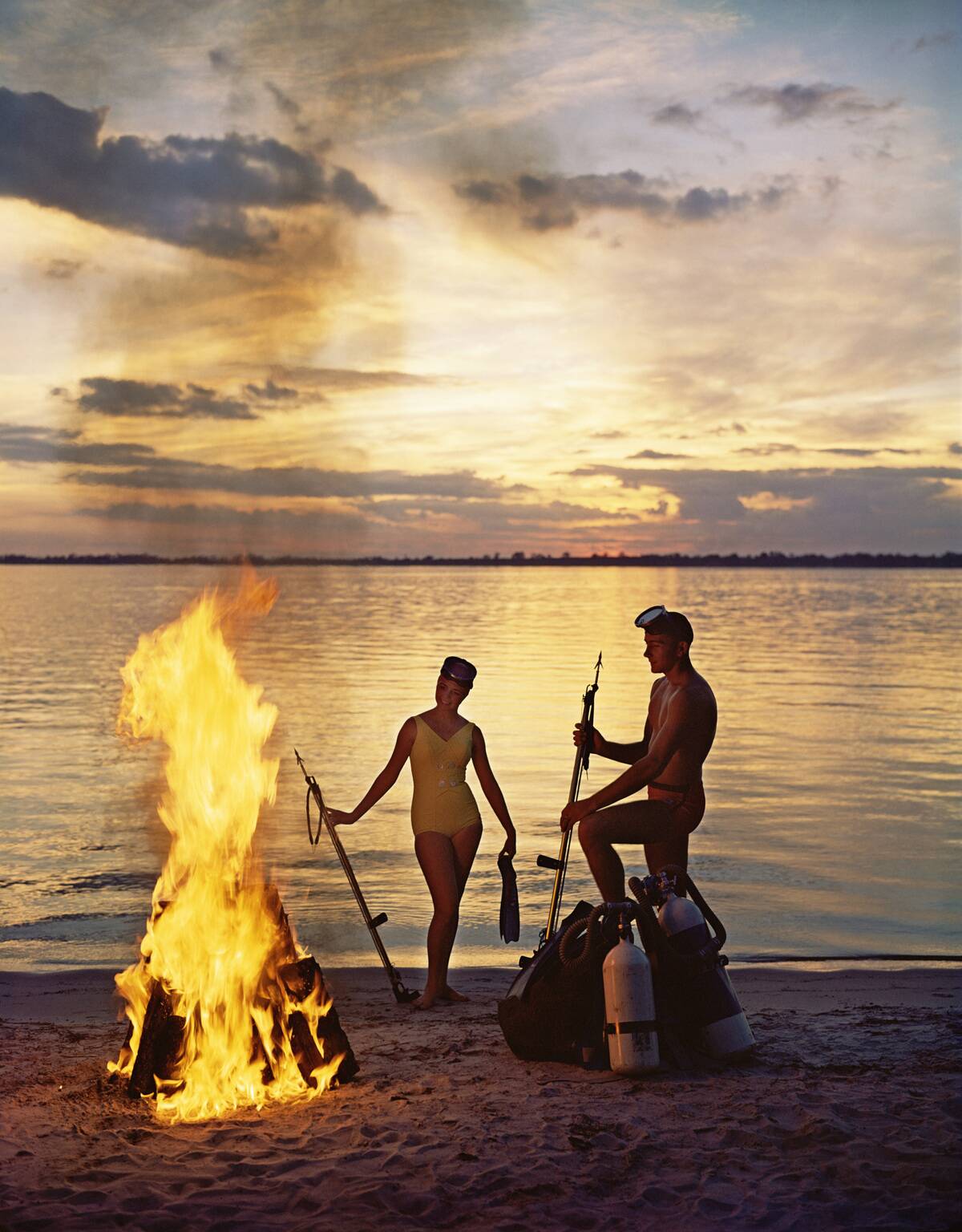 Young couple of skin divers relaxing at bon fire on beach