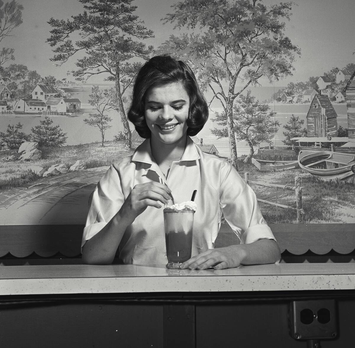 A young girl excited to have milkshake at diner counter in front of large artwork